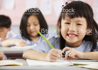 Young Female Student Working At Desks In Chinese School Classroom Smiling To Camera