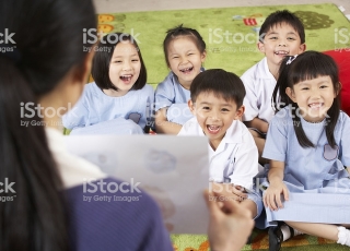 Teacher Showing Painting To Students In Chinese School Classroom Sitting Down Smiling