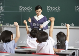 Students In A chinese School Classroom Putting Up Their Hands To Answer The Teacher